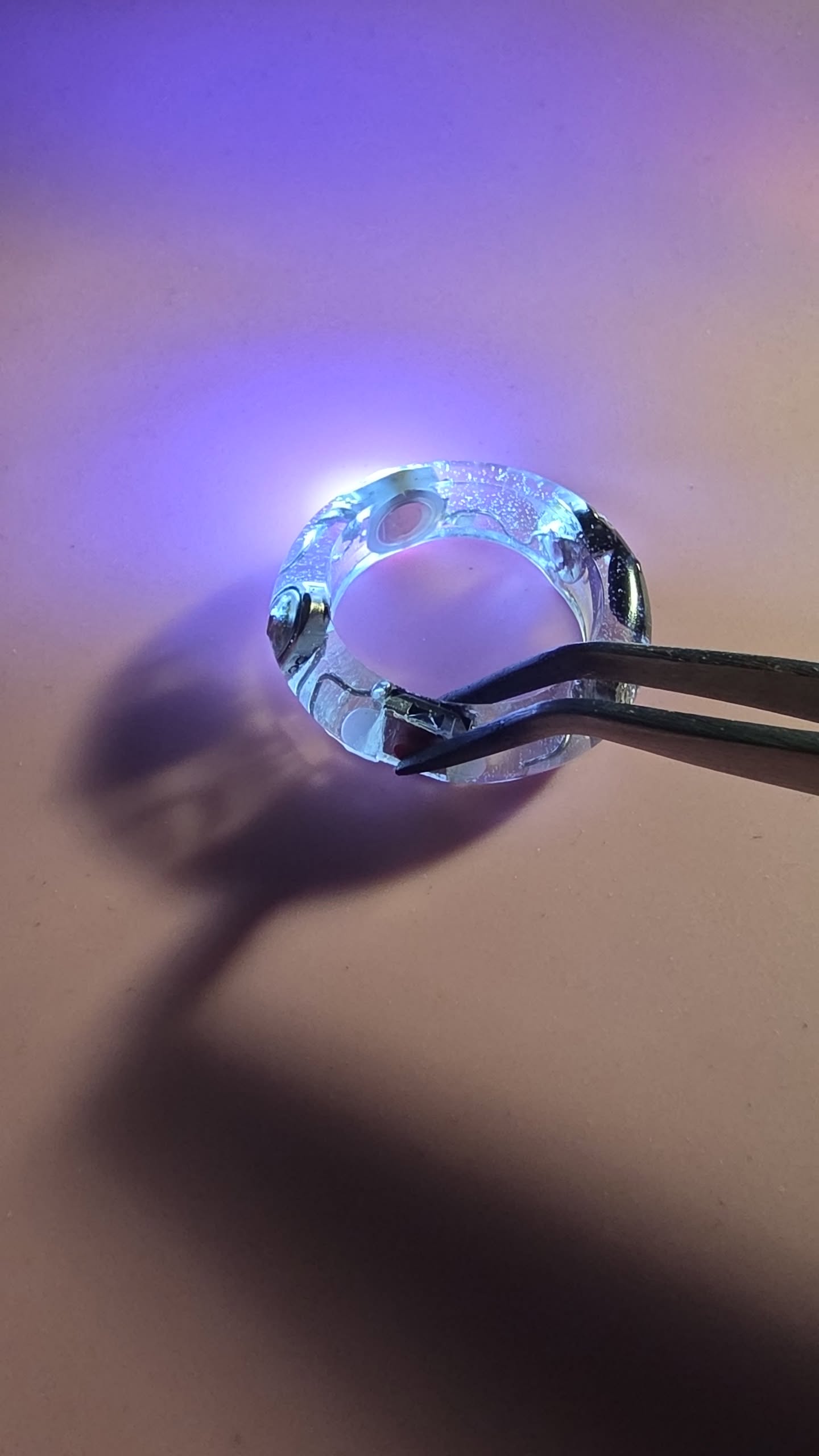 Light Ringz Prototype No. 1 — The Original, clear resin ring glowing blue/purple held with tweezers